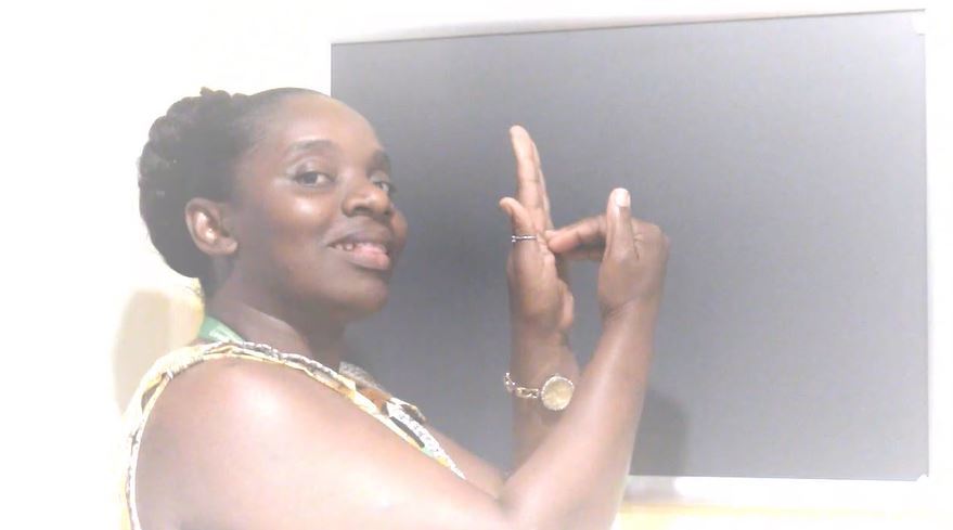 Shaunette looks at the camera while she is signing the letter "Z" using both hands.